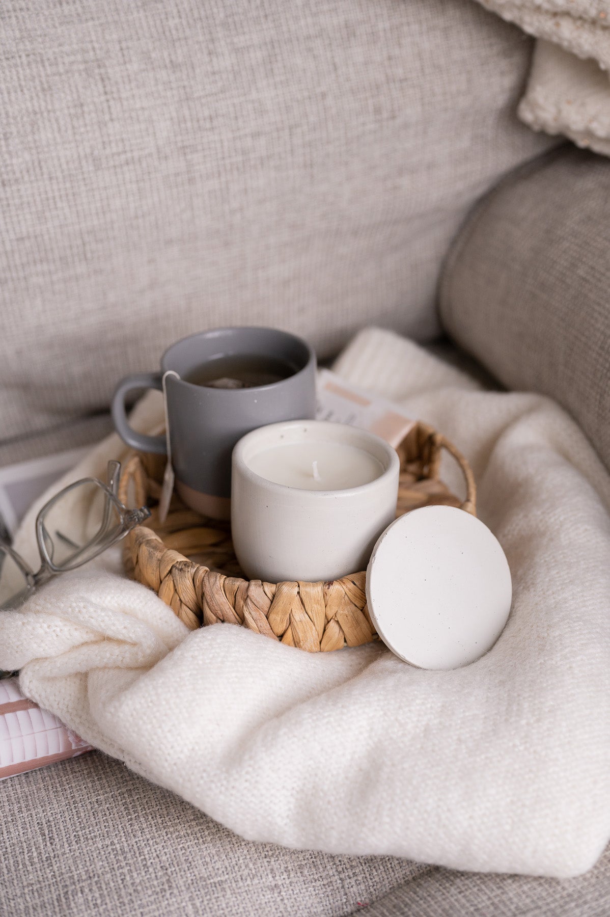 white noura blanc candle on neutral couch with gray mug and cozy vibes