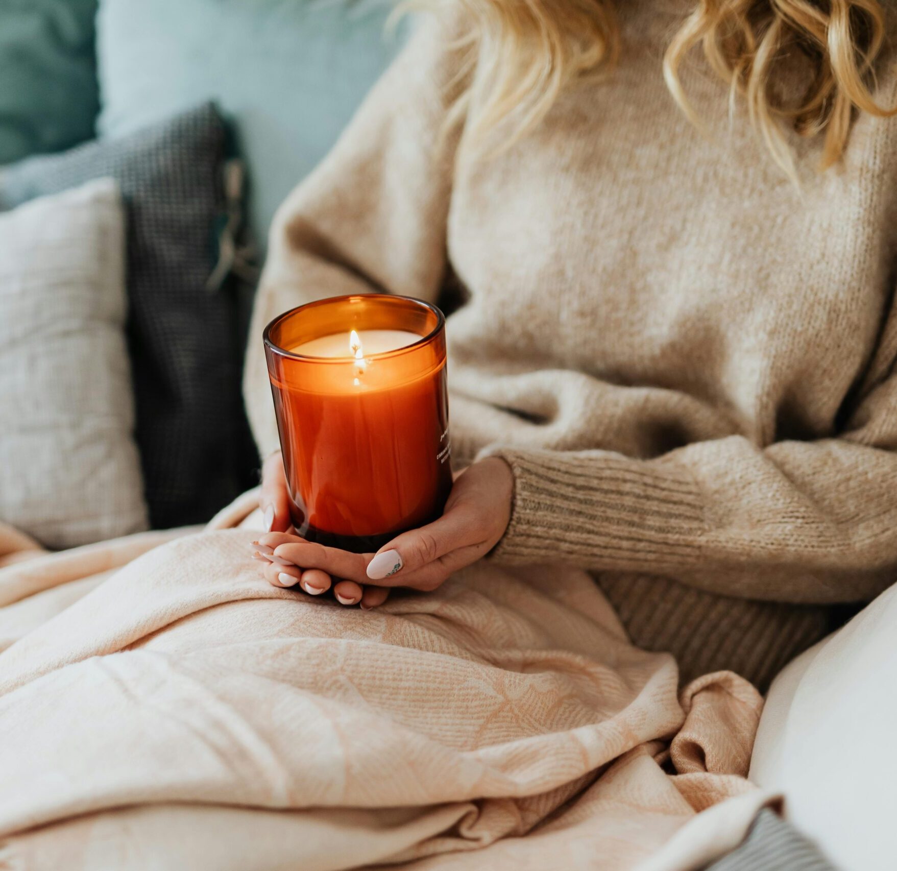 woman holding lit candle and sitting on cozy bed